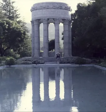 Pulgas Water Temple reflected in a still reflecting pool, with a lone person standing nearby.
