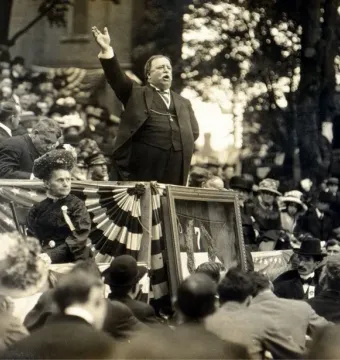 William Howard Taft speaks from a raised platform at the unveiling of the George Armstrong Custer Equestrian Monument, with crowd and bunting below.