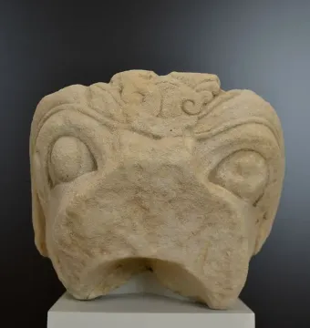 Grifo de Redován stone head sculpture with rounded eyes and a beak-like mouth on a pedestal.