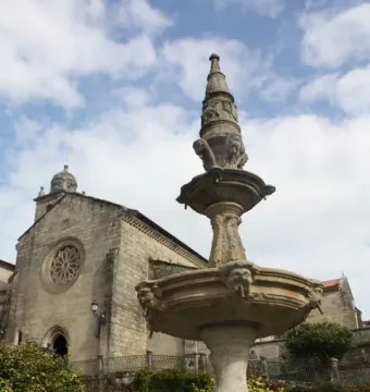 Herrería Fountain in a shallow green-tinged pool, with a stone building and rose window in the background.