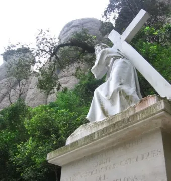Monumental Rosary of Montserrat statue of a robed figure carrying a large cross on a pedestal.