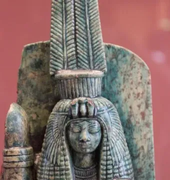 Bust of Queen Tiye with a tall segmented headdress and broad wig, holding an arched object.
