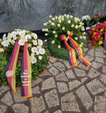 Floral wreaths with German tricolor ribbons rest on the cobblestones at the Memorial to the Murdered Sinti and Roma of Europe, beside a reflective water basin marked with the name Libau.