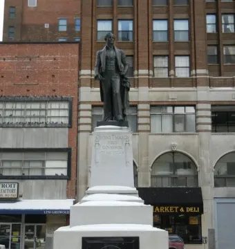 Stevens T. Mason Monument on a snowy stone pedestal beside downtown buildings.