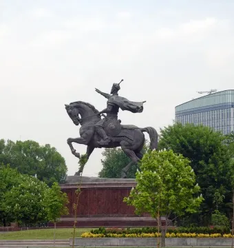 Timur equestrian statue on a reddish-brown pedestal surrounded by trees and flowers.