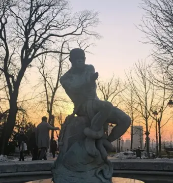 Fisherman Fountain bronze statue of a man wrestling a serpent on a dark fountain base at dusk.