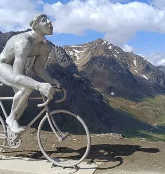 Géant du Tourmalet statue of a muscular cyclist on a mountain overlook with snowy peaks in the background