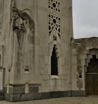 Relief carvings and decorative stonework on the National Shrine of the Little Flower tower, with a bronze double door in a stepped archway.