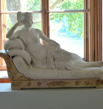 Venus Victrix, a reclining white marble woman on an ornate chaise lounge by a window.