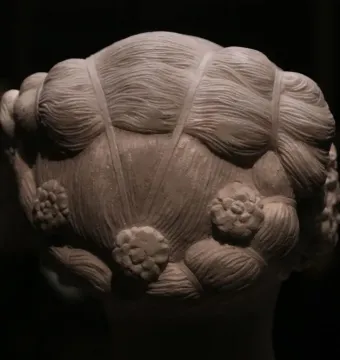 The back of Verrocchio\'s Bust of a Young Woman, showing an intricately carved hairstyle with waves, bands, and floral rosettes.
