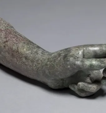 Detached bronze hand and forearm from the Cleveland Apollo, with a green and reddish-brown patina and curled fingers.