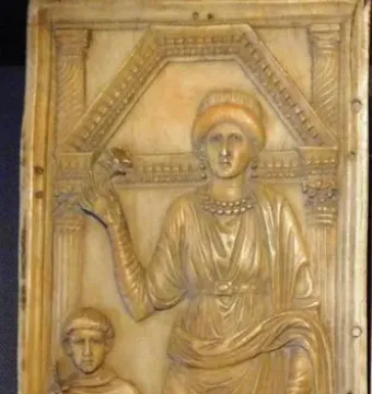 Carved relief from the Diptych of Stilicho showing two standing figures beneath an architectural canopy, with a taller robed figure holding an object aloft beside a smaller figure with a book or scroll.