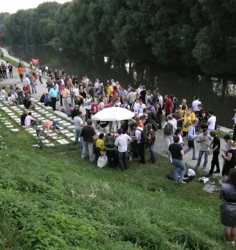 Crowd gathered around the Keyboard Monument, a land-art installation made of rectangular blocks on a grassy slope beside the river.