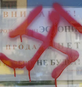 A red swastika spray-painted over a white Russian sign behind reflective glass.