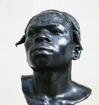 Dark metallic bust of an Aruwimi native with textured hair, a prominent nose, and an earring on a square base.
