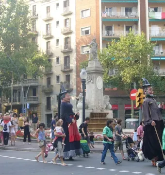 The Fountain of Hercules stands in a city square with oversized costumed figures and pedestrians around the base.