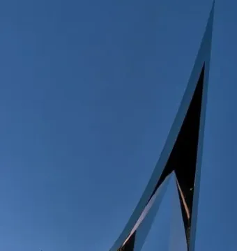 The Life Electric sculpture in Como, a tall reflective silver monument against a deep blue twilight sky and waterfront lights.