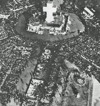 A large crowd gathers around the Monument to the Carta Magna and Four Regions of Argentina, with a tall cross rising from the top of the monument.