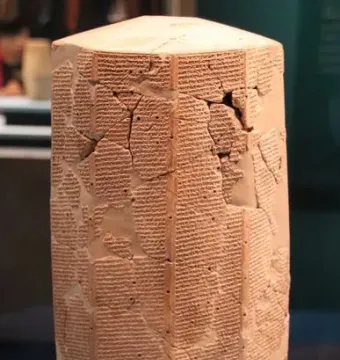 Rassam cylinder covered with dense rows of cuneiform script on a reddish-brown multi-sided prism with visible cracks and missing fragments.