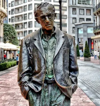 Woody Allen memorial statue in Oviedo, showing a bronze man wearing glasses, an open-collared shirt, and a jacket.