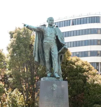 Benito Juarez bronze statue in formal attire, pointing forward and holding a scroll on a stone pedestal.