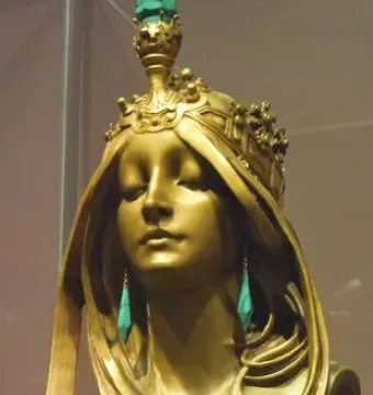 Polished bronze bust of a woman with closed eyes, wearing an ornate crown and long teal earrings.