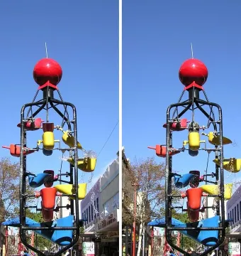 The Bucket Fountain sculpture with colorful tipping buckets spraying water against a blue sky.