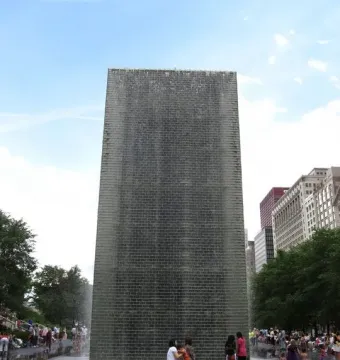 Crown Fountain in Chicago with water cascading down a tall tower as people gather around the reflective pool.