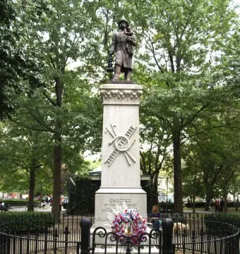 Firemen\'s Monument showing a bronze rescuer holding a child atop a tall stone pillar inside a fenced area.