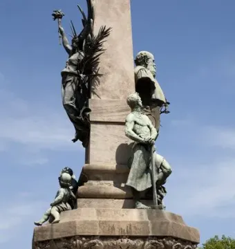 Rius i Taulet Monument with bronze figures and reliefs on a stone column.