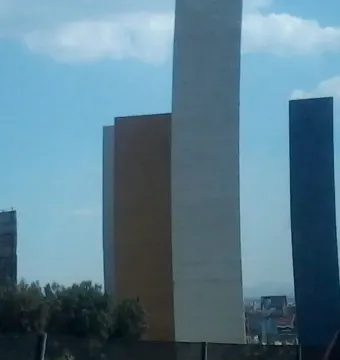 Torres de Satélite with three tall colored rectangular towers against a partly cloudy blue sky.