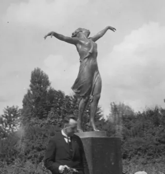 The Dancing Girl statue on a pedestal outdoors, with a man standing near the base among greenery.