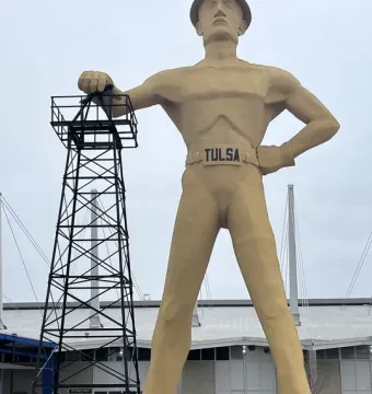 Golden Driller statue standing beside an oil derrick model in Tulsa