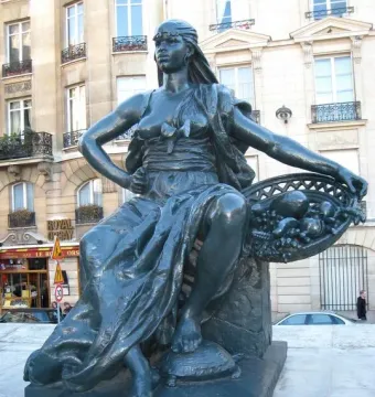 L\'Afrique by Eugène Delaplanche, a dark statue of a seated woman with a headwrap holding a basket of fruit, with one foot resting on a turtle.
