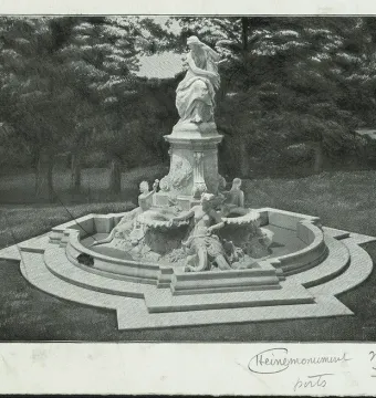 The Lorelei Fountain, a stone fountain with a standing figure on a tall pedestal and smaller figures in a stepped basin, set in a wooded park.