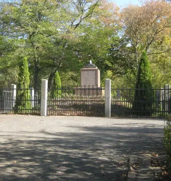Napoleonstein stone pillar behind a black metal fence in a sunny park.