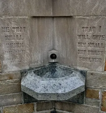 Stone holy water font at the National Shrine of the Little Flower with a metal spigot and carved inscription.