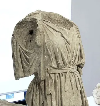 Heavily damaged headless and armless torso of Athena and Marsyas, displayed on metal supports in a museum.