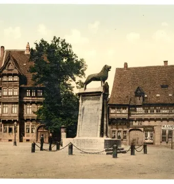 The Brunswick Lion stands on a tall stone pedestal in a town square, surrounded by a chain fence.