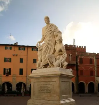 Canapone monument with a central standing male figure, seated female figure, and children on a tall stone pedestal in a town square.
