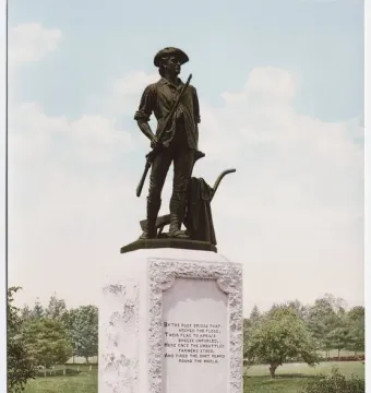 The Minute Man bronze statue of a colonial militiaman holding a musket beside a plow on a stone pedestal in a park.