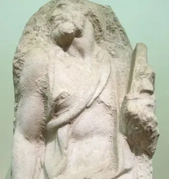 Saint Matthew sculpture carved from a rough stone block, with the figure emerging in a strained pose.