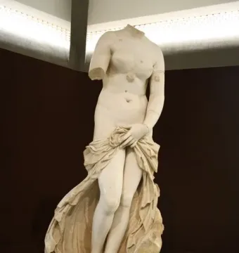 Headless marble Venus Landolina statue with one arm missing, draped cloth around her lower body, standing on a pedestal with an information plaque.