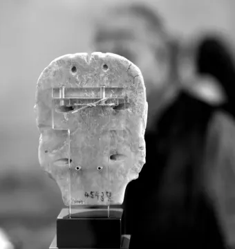 Back view of the Warka Mask on a display stand with acrylic supports and visible repairs.
