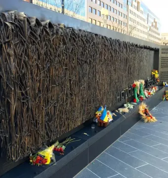 Holodomor Memorial bronze wall with a relief of wheat stalks, flowers, candles, and small Ukrainian flags at the base.