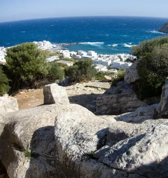 The Kouros of Apollonas lies unfinished in a rocky quarry overlooking the sea and coastal buildings.