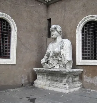 Madama Lucrezia stone bust on an ornate pedestal beside arched windows in a weathered wall.