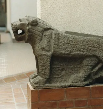 Maraş lion stone sculpture with an open mouth, carved in low relief and set on a brick pedestal.