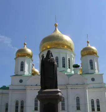 Monument to Dimitry of Rostov in front of a white cathedral with golden domes and crosses.