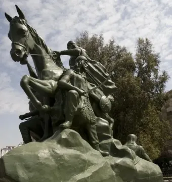 Low-angle view of the Saladin equestrian statue, showing a bronze warrior on a rearing horse above smaller figures on a rock-like base.